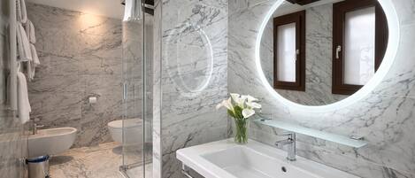 A modern bathroom with a glass shower enclosure, a white sink, and a marble-tiled wall.