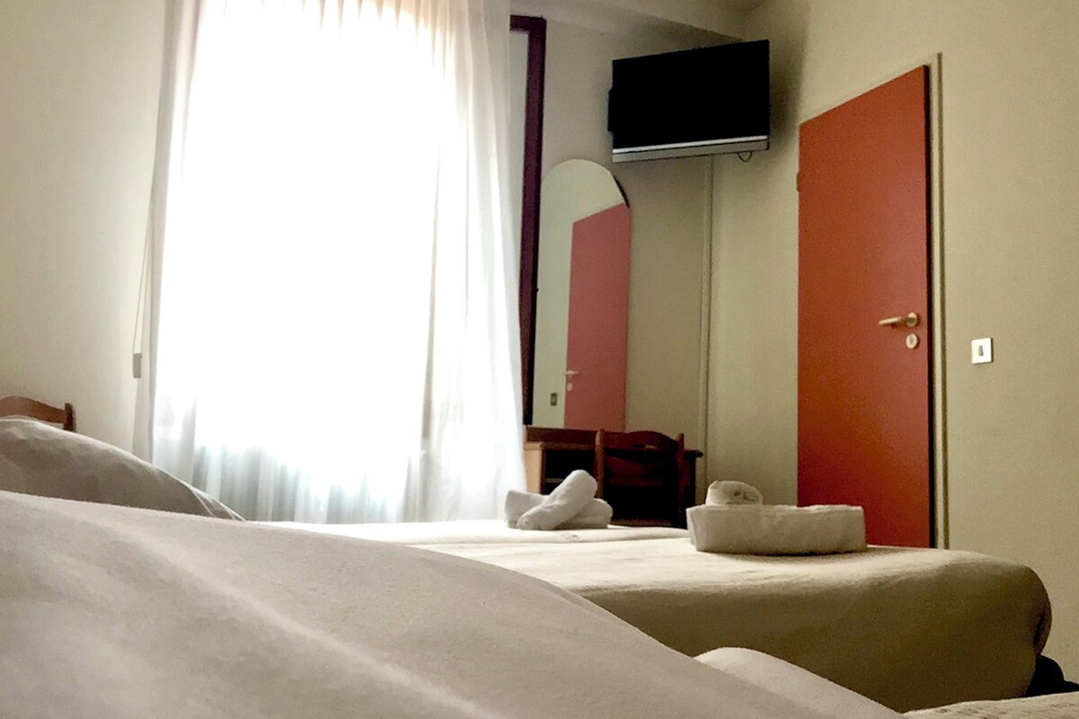 Habitación de hotel con dos camas, un televisor montado en la pared y un espejo grande.