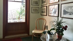Una habitación con puerta de madera, una silla de mimbre, una planta en maceta y varias fotografías enmarcadas en la pared.