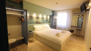 Una habitación de hotel moderna con una cama grande, mesitas de noche, una pequeña mesa redonda, un banco, un espejo y una pared con un mural náutico.