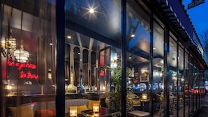 L’extérieur d’un hôtel, avec de grandes fenêtres, des places assises en plein air et un panneau lumineux au néon.