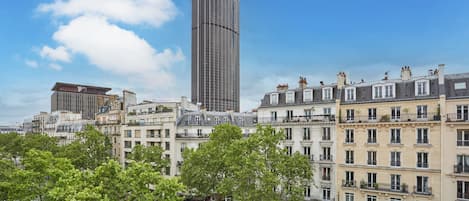 Un paisaje urbano con un edificio moderno alto, edificios tradicionales de varios pisos y árboles verdes.