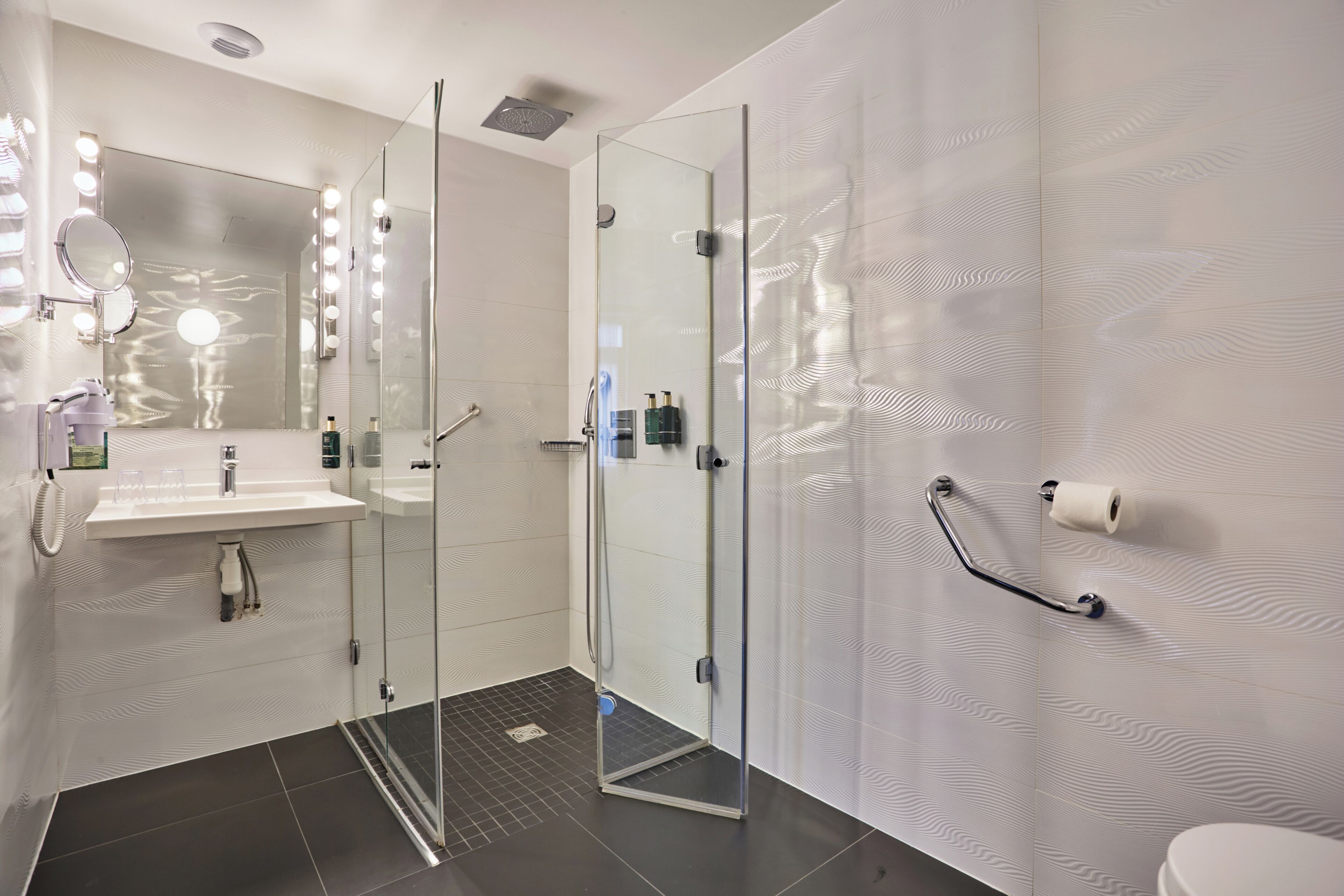 Een moderne badkamer met een douchecabine van glas, een wastafel met spiegel en verlichting, en een toilet met een handgreep.