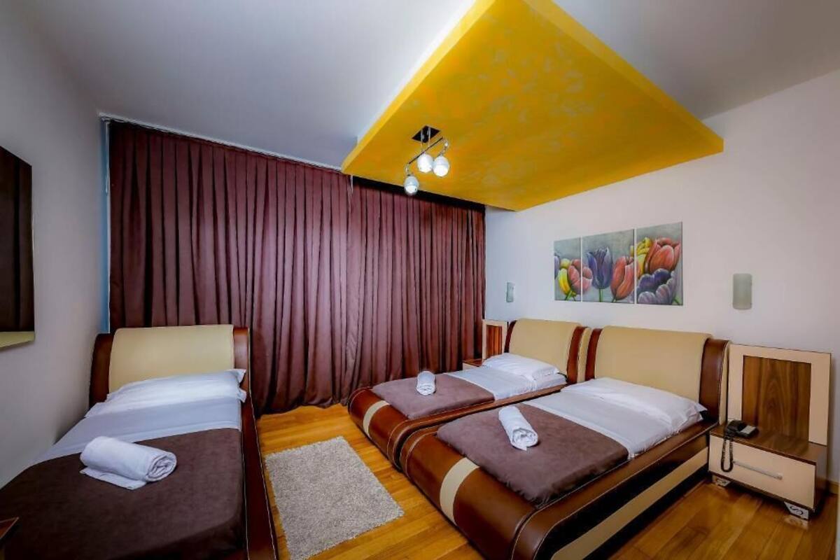 Habitación de hotel con dos camas, suelo de madera, un ventanal grande con cortinas y una lámpara en el techo.