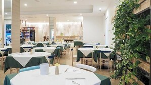 A restaurant with multiple tables, chairs, and a green plant wall.