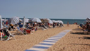 A beach with striped umbrellas, lounge chairs, and a clear view of the sea. - Hotel Moderno (Jesolo)
