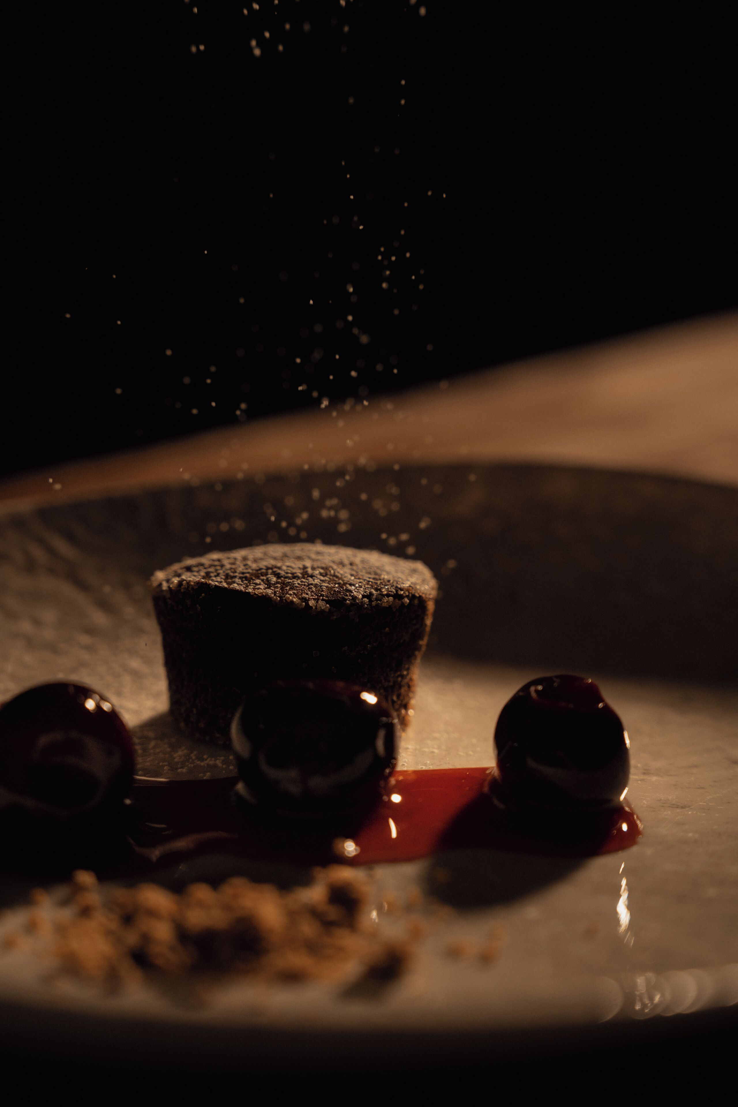 A dessert with a dusting of powdered sugar, a red sauce, and a dark chocolate piece on a plate.
