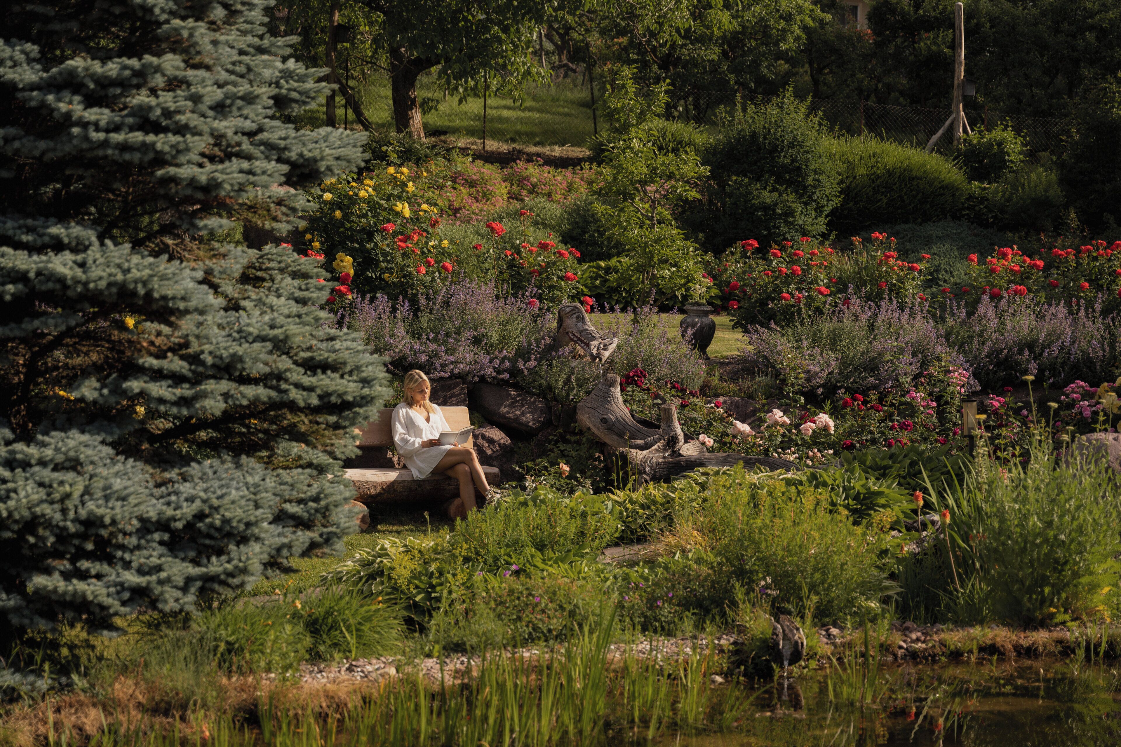 A woman sitting on a bench in a garden with various plants and flowers.