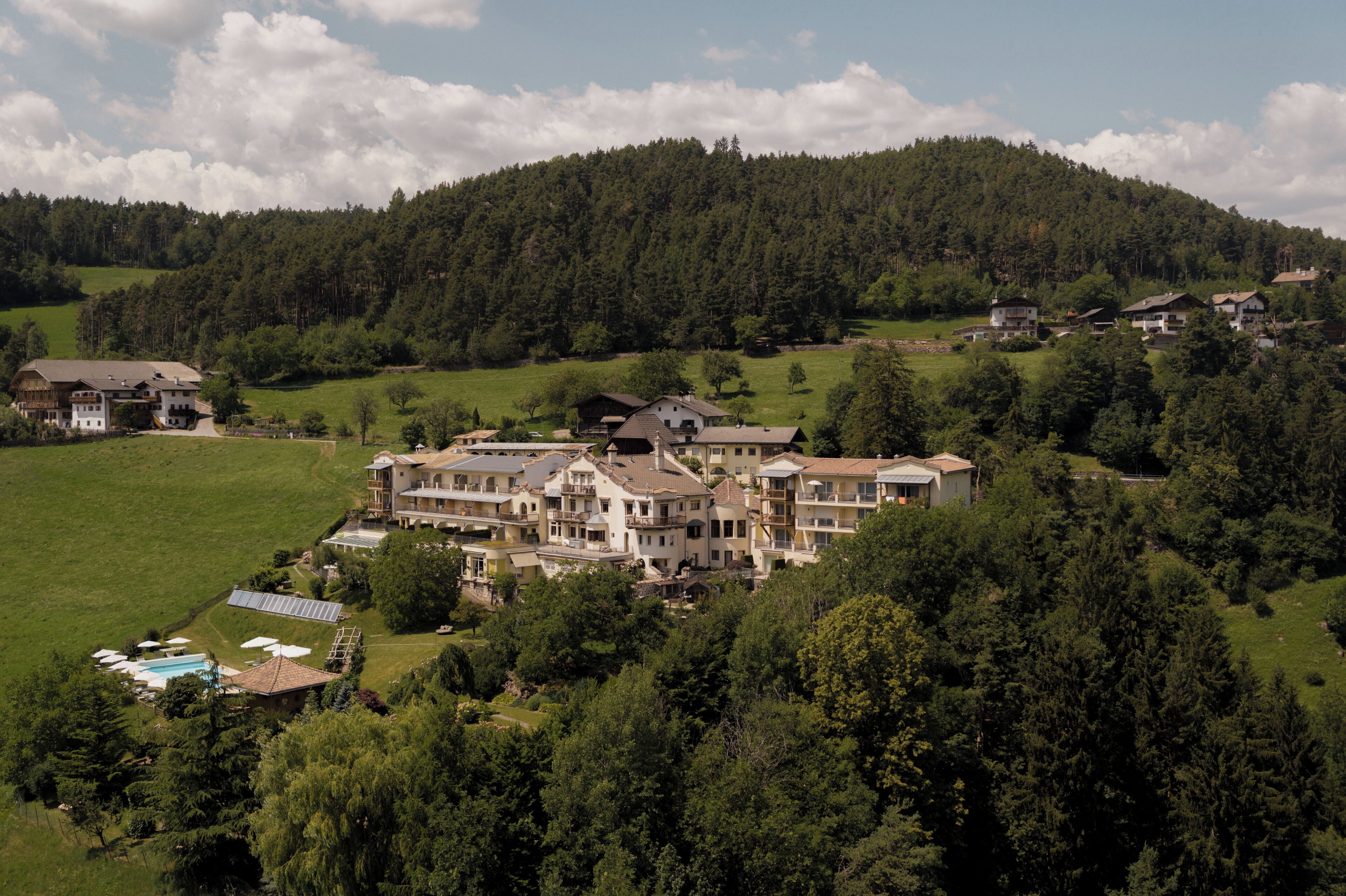 Um hotel grande, com vários andares e uma estrutura de telhado elaborada, rodeado por vegetação exuberante e uma paisagem acidentada.