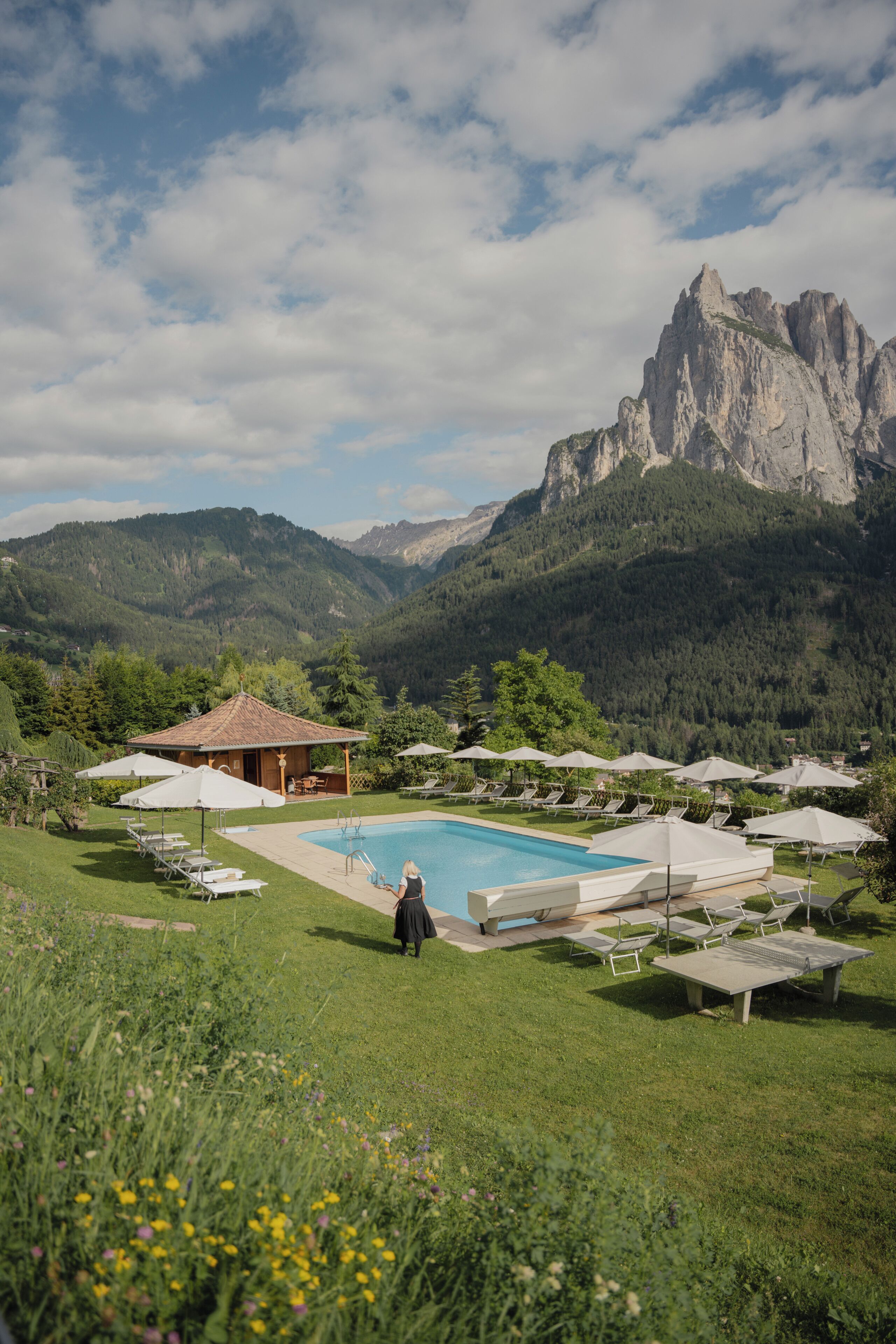 Ein Poolbereich mit Liegestühlen und Sonnenschirmen, umgeben von einer gebirgigen Landschaft.