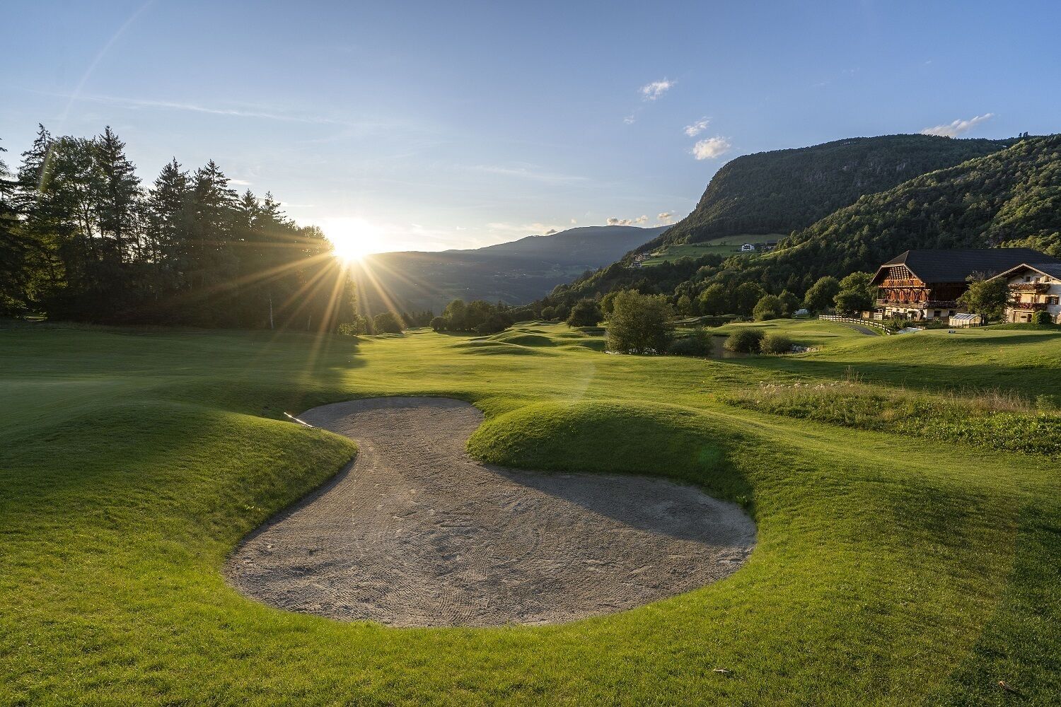 A golf course with a sand trap, a house, and a mountain in the background.