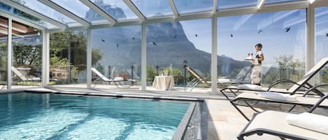 A swimming pool with lounge chairs and a glass-enclosed area with mountain views.