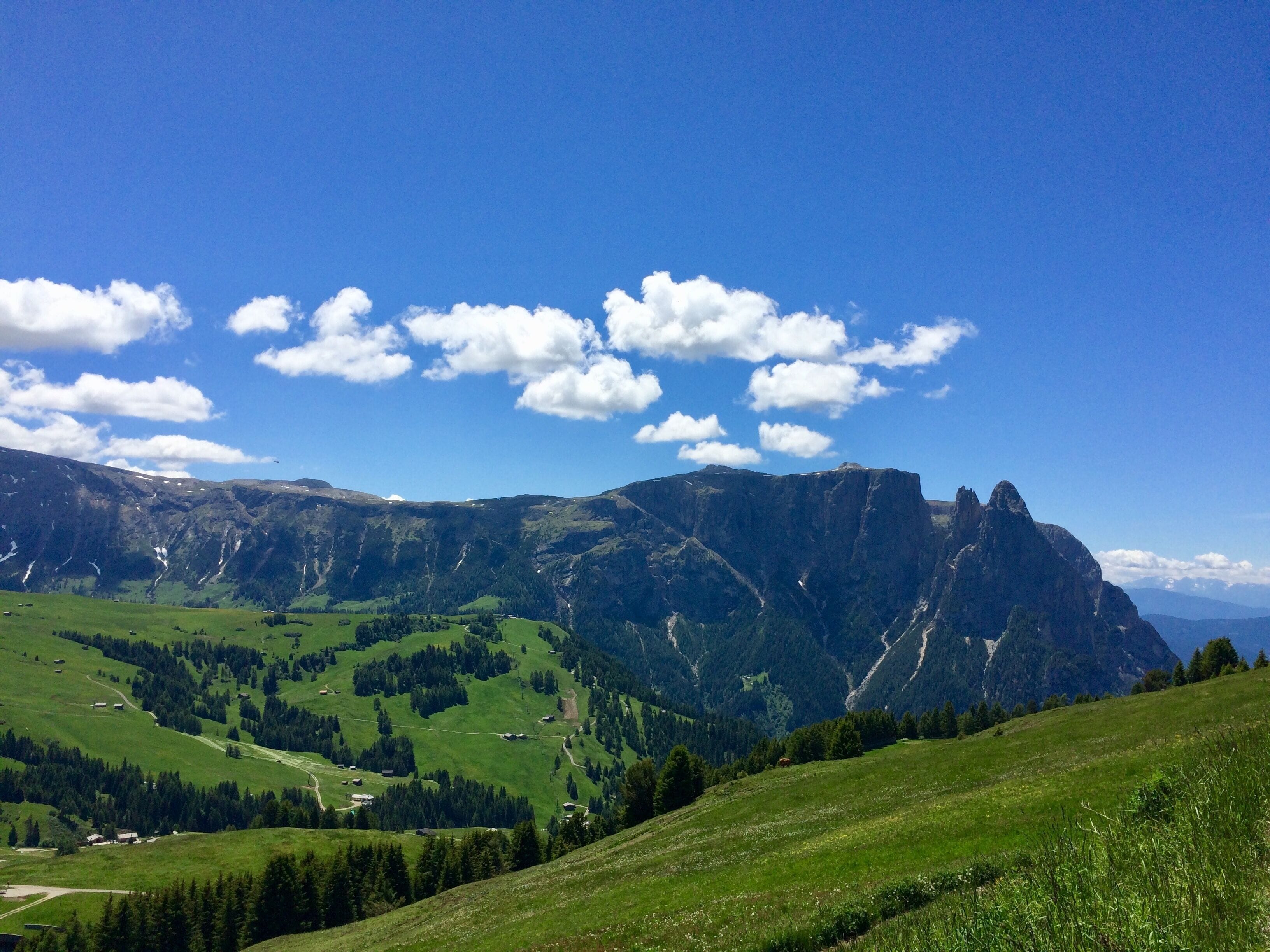 Eine Berglandschaft mit grünen Feldern und felsigen Klippen unter blauem Himmel.
