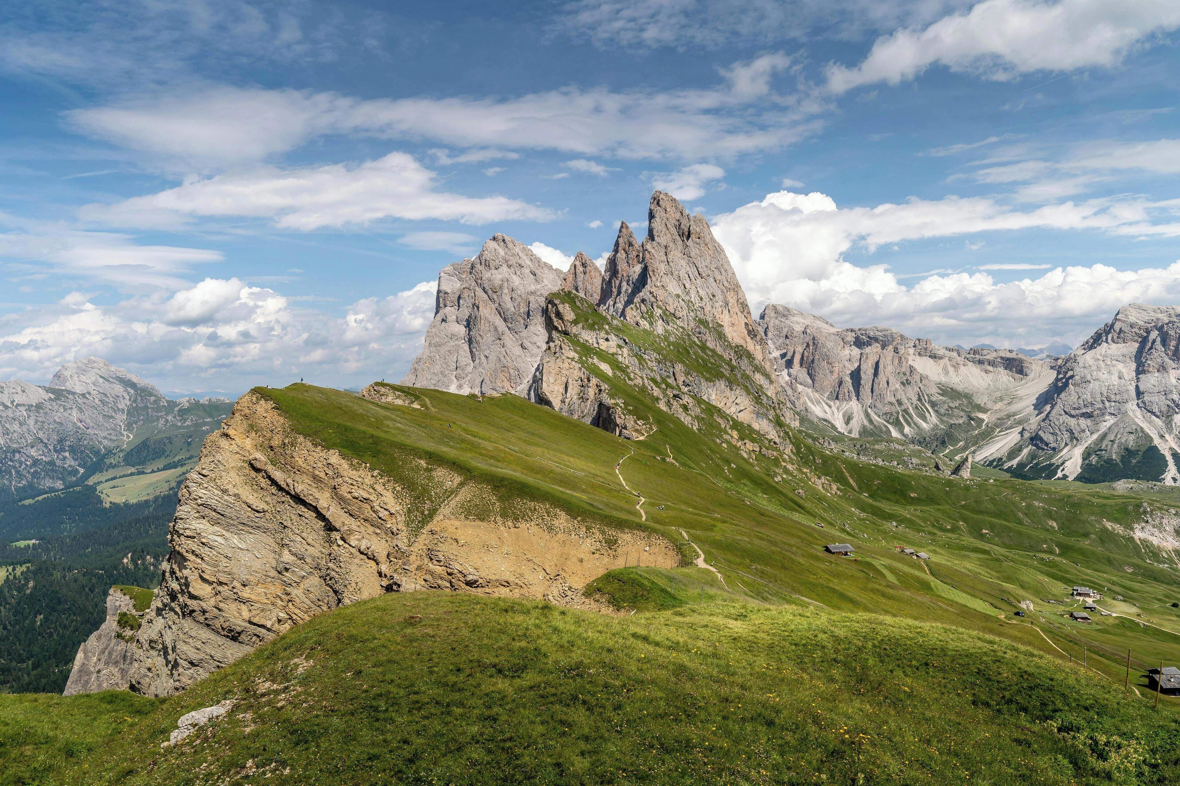 Un paysage montagneux caractérisé par un sommet rocheux imposant, un sentier sinueux et des bâtiments dispersés.