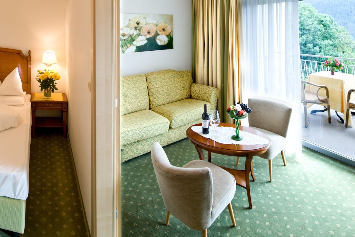 A hotel room with a bed, a green sofa, a dining table, and a balcony with a view.