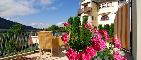 A balcony with outdoor furniture and vibrant pink flowers, overlooking a mountainous landscape.