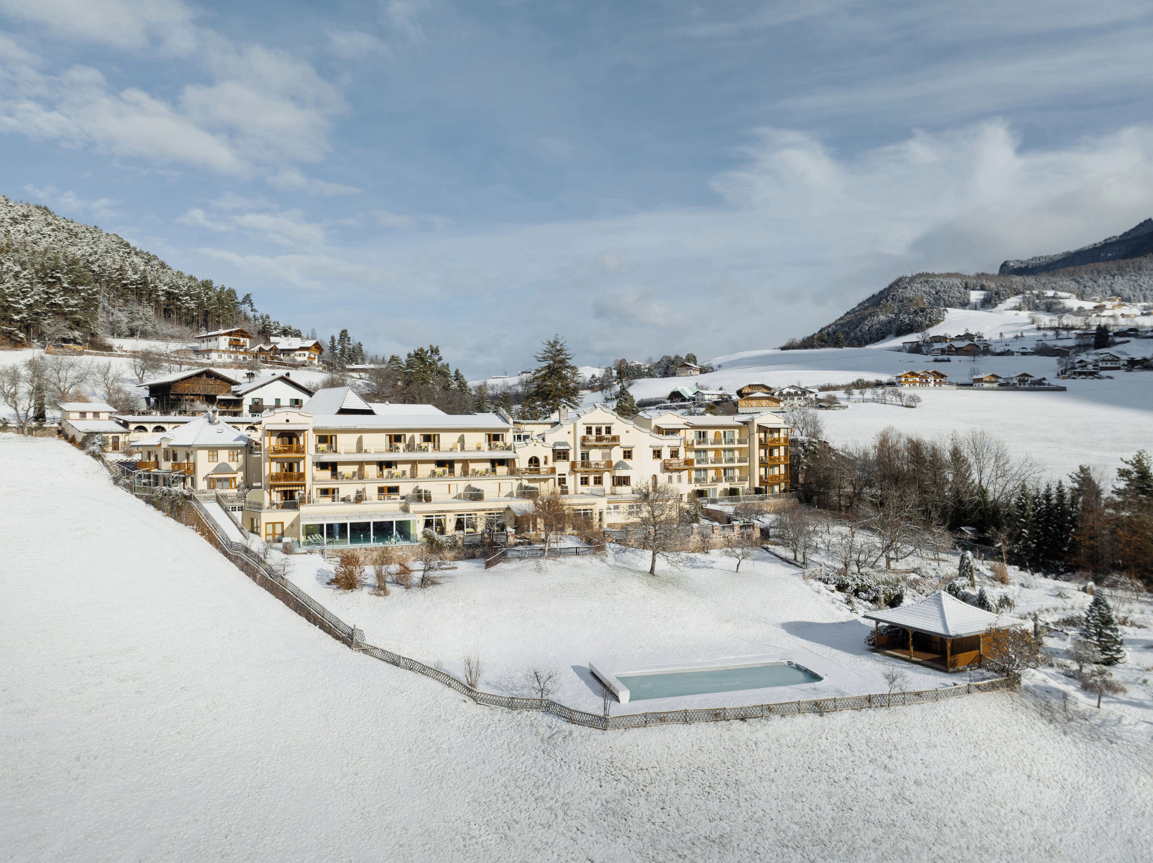 Estância coberta de neve com vários edifícios, piscina e montanhas ao fundo.