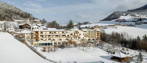 Un complejo turístico nevado con varios edificios, una piscina y montañas al fondo.