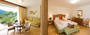 Habitación de hotel con cama, zona de estar con sofá y sillones, mesa de comedor con una silla, y vistas al exterior.
