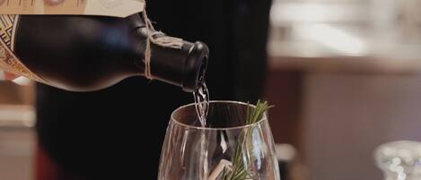 A person pouring a drink from a bottle into a glass with ice and a sprig of rosemary.
