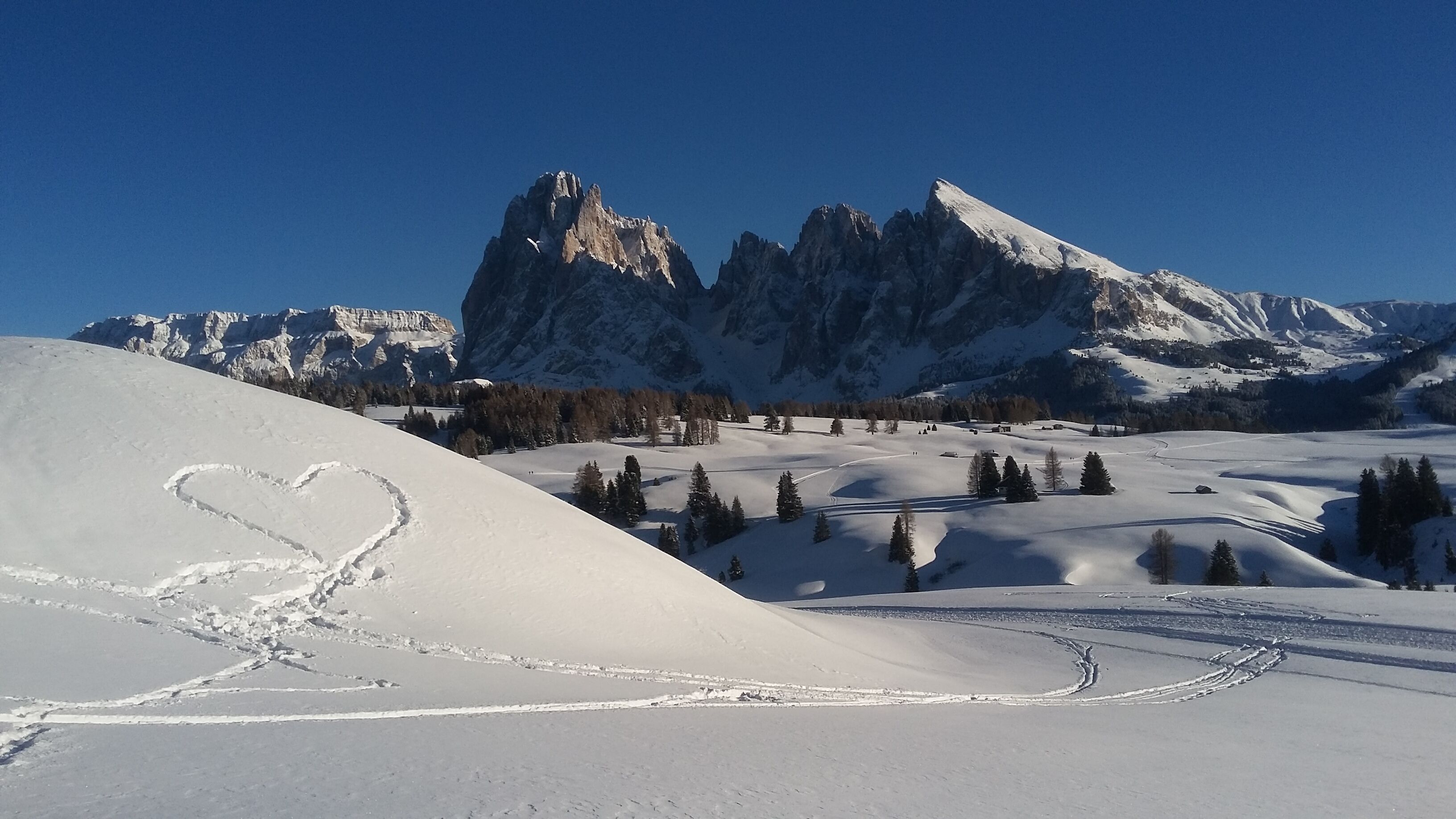 Eine verschneite Berglandschaft mit einem herzförmigen Schneemuster und einer Skipiste.