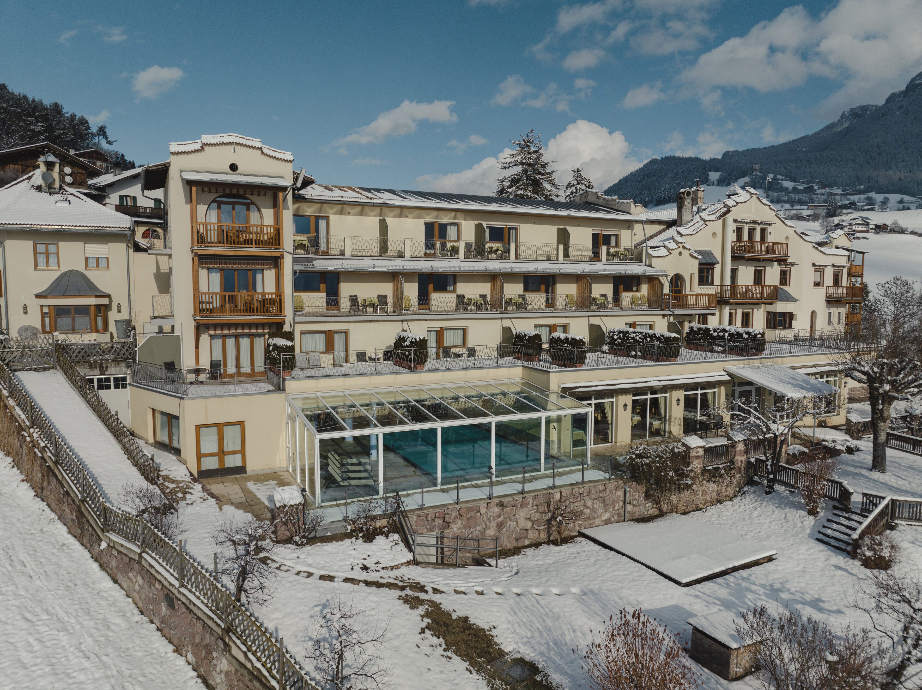 Ein mehrstöckiges Hotel mit Pool in Glasarchitektur, schneebedeckter Umgebung und Bergkulisse.