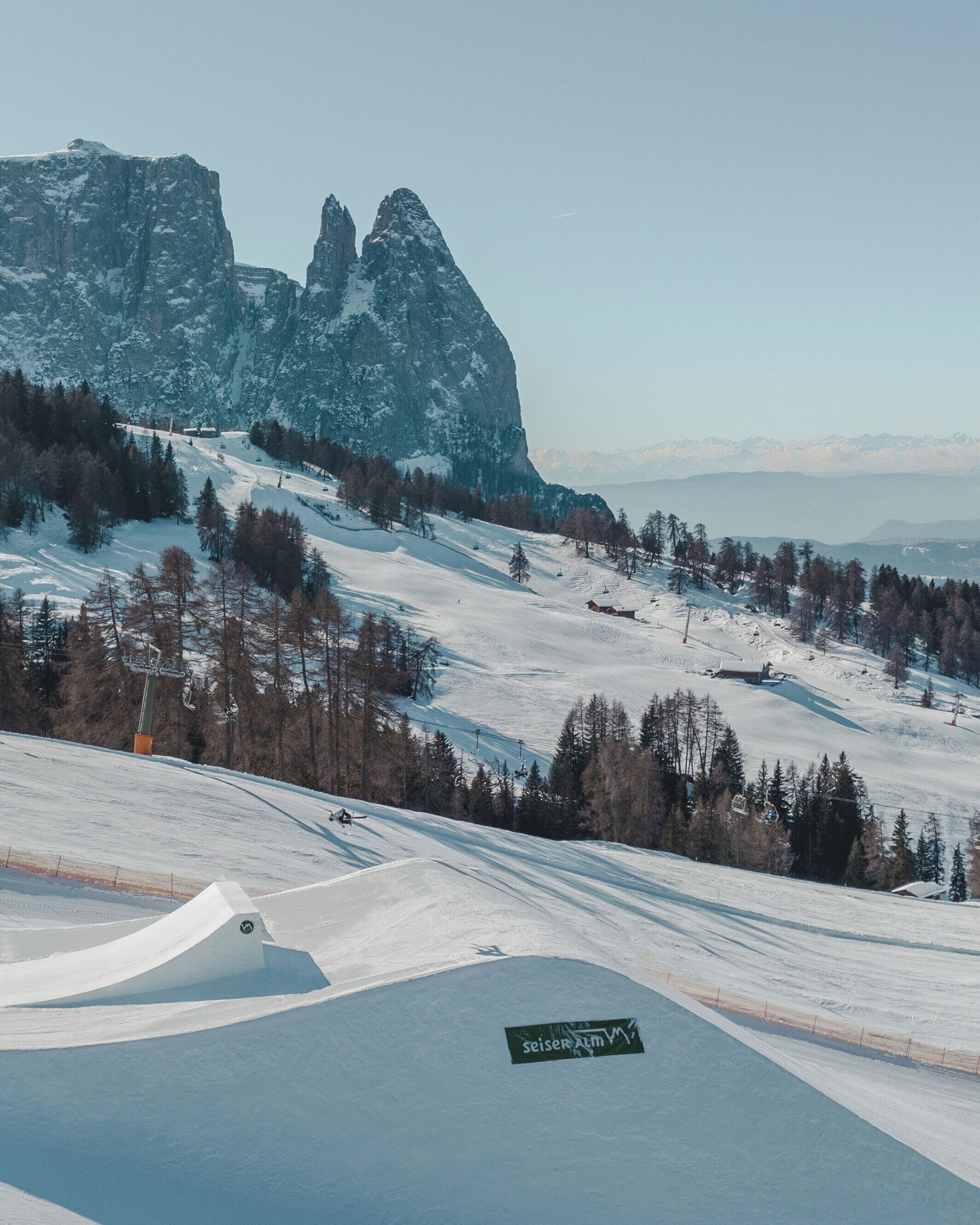 A snow-covered ski slope with a ski lift and a mountain backdrop.