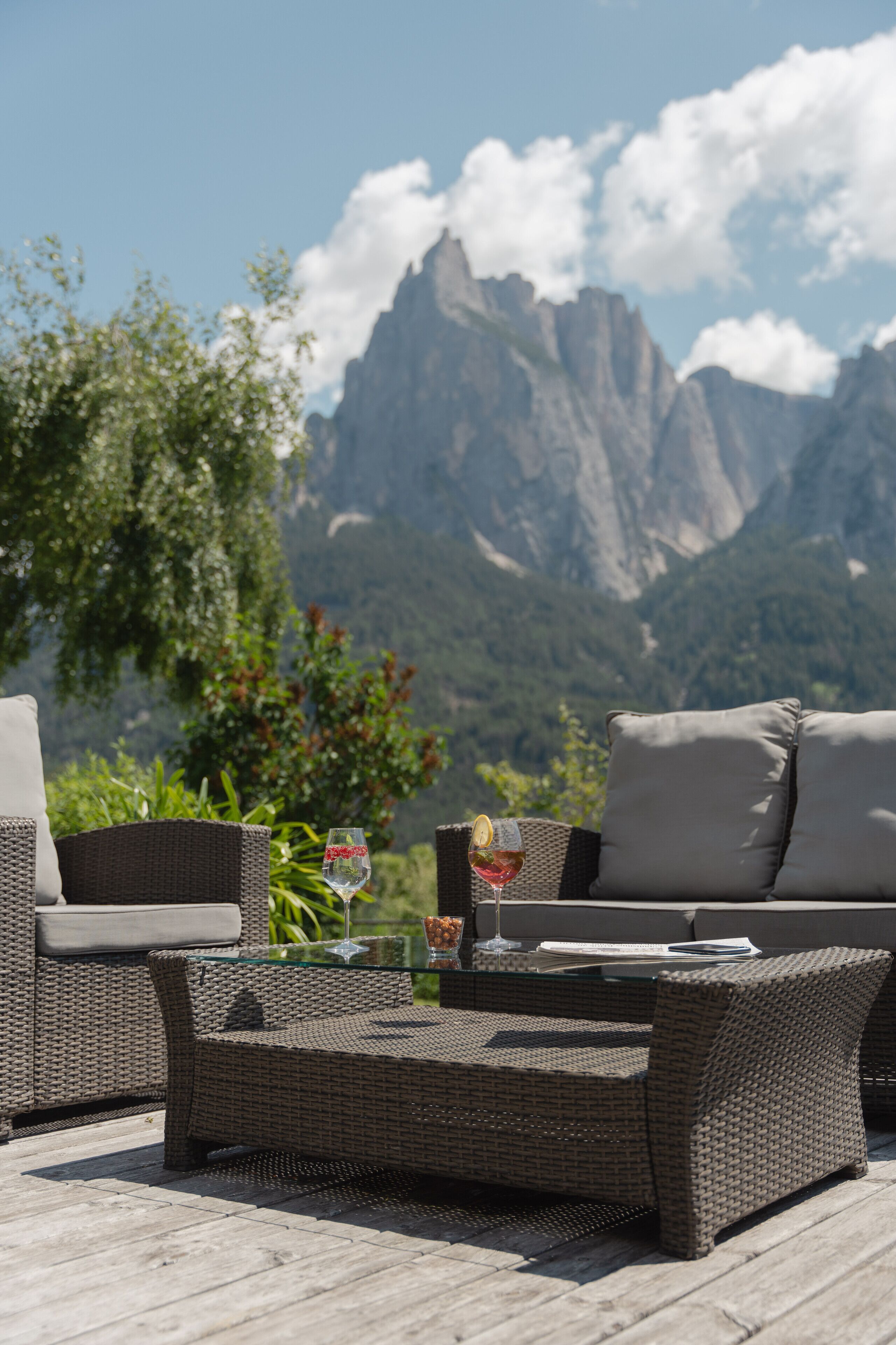 Un área de estar exterior de ratán con una mesa de vidrio, dos cojines y una copa de vino.