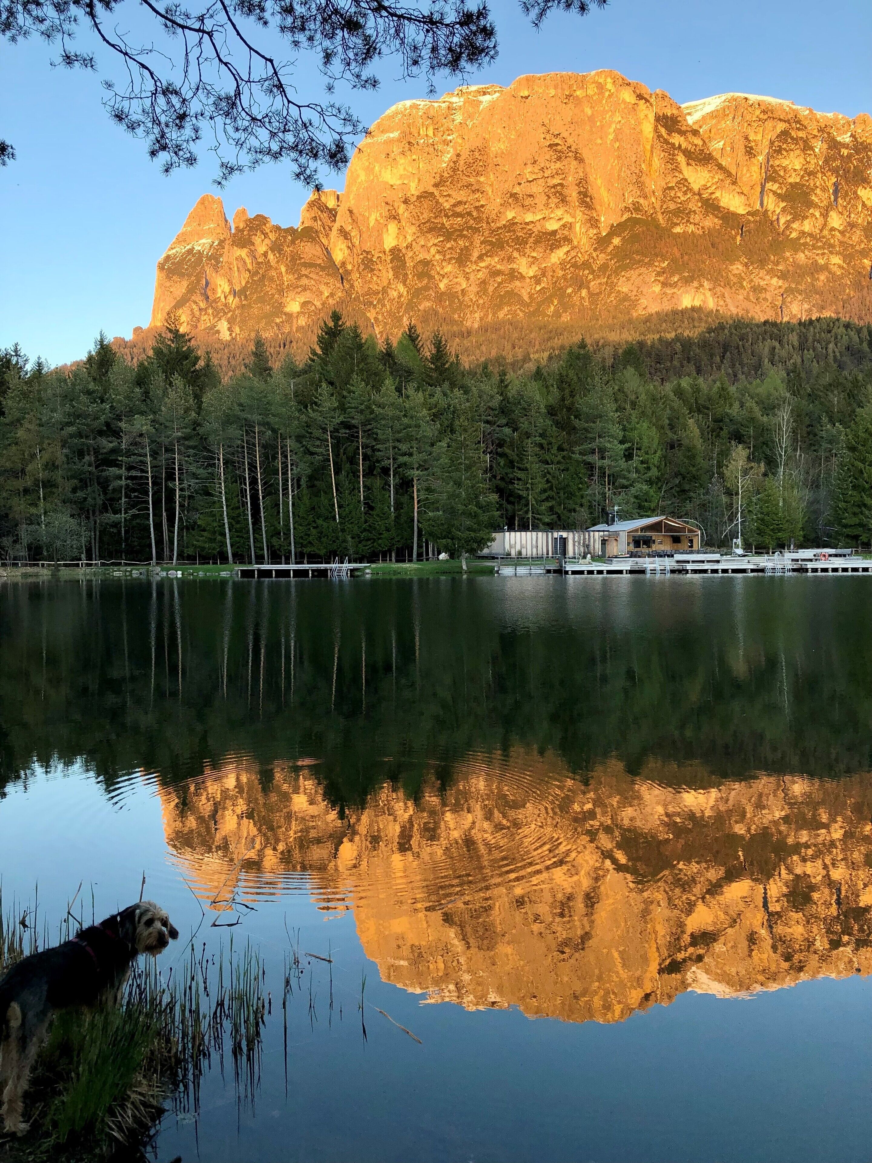 Un llac amb una muntanya al fons, un moll i una cabana.