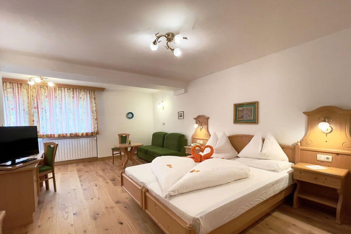A hotel room with a wooden bed, a desk with a television, a green armchair, and a window with curtains.
