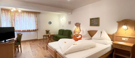 A hotel room with a wooden bed, a desk with a television, a green armchair, and a window with curtains.