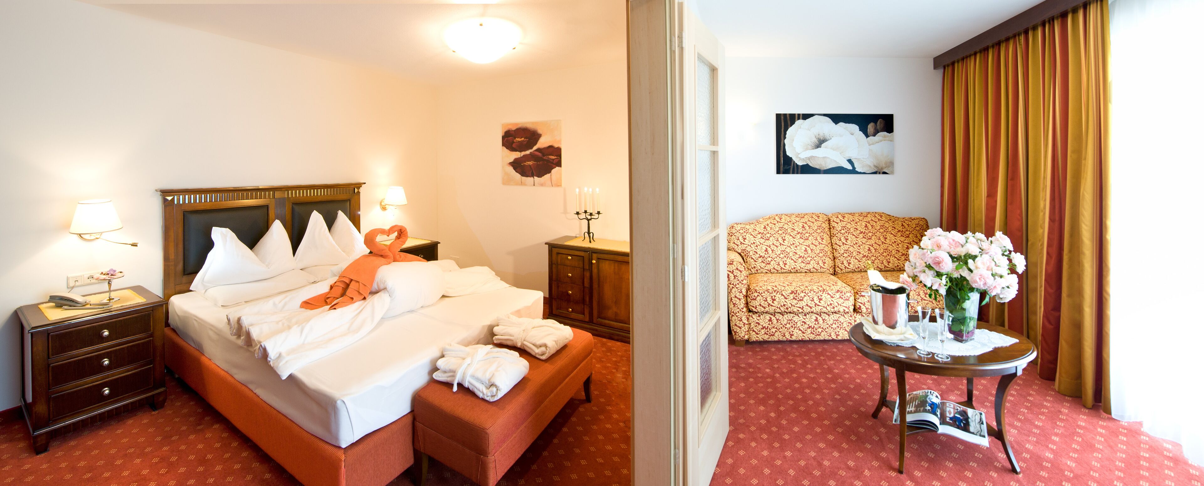 A hotel room with a bed, nightstands, a table with flowers, and a sofa.