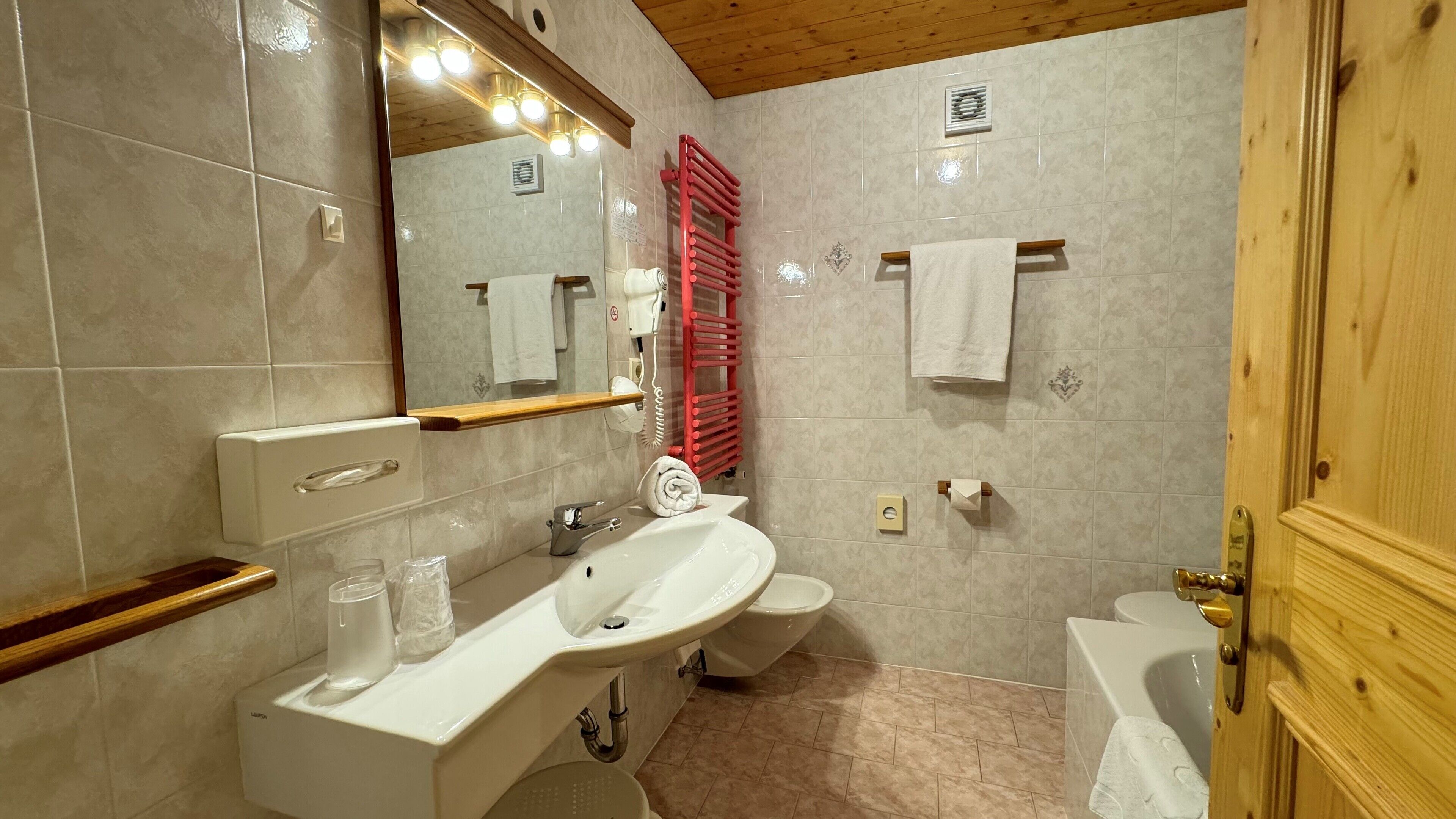 A bathroom with a sink, mirror, toilet, and a red towel rack.