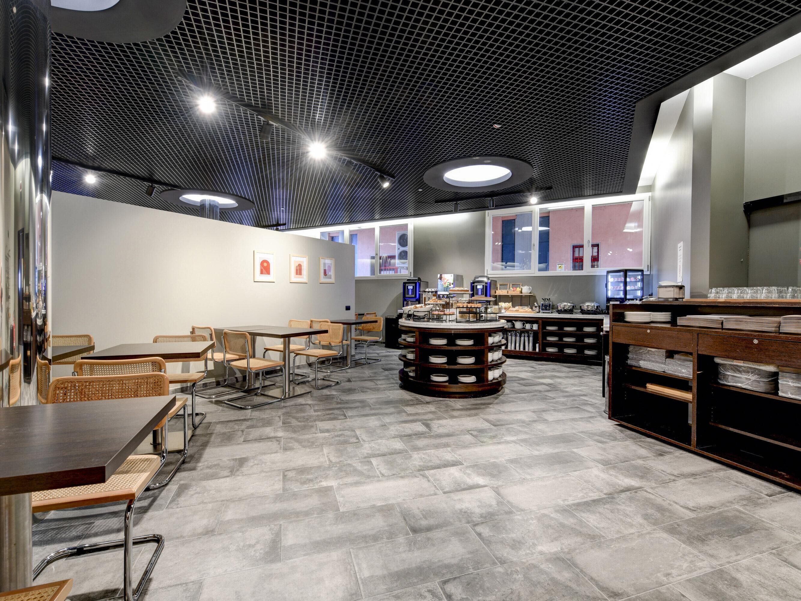 A modern cafe with a herringbone floor pattern, round tables, and a central island with a coffee station.