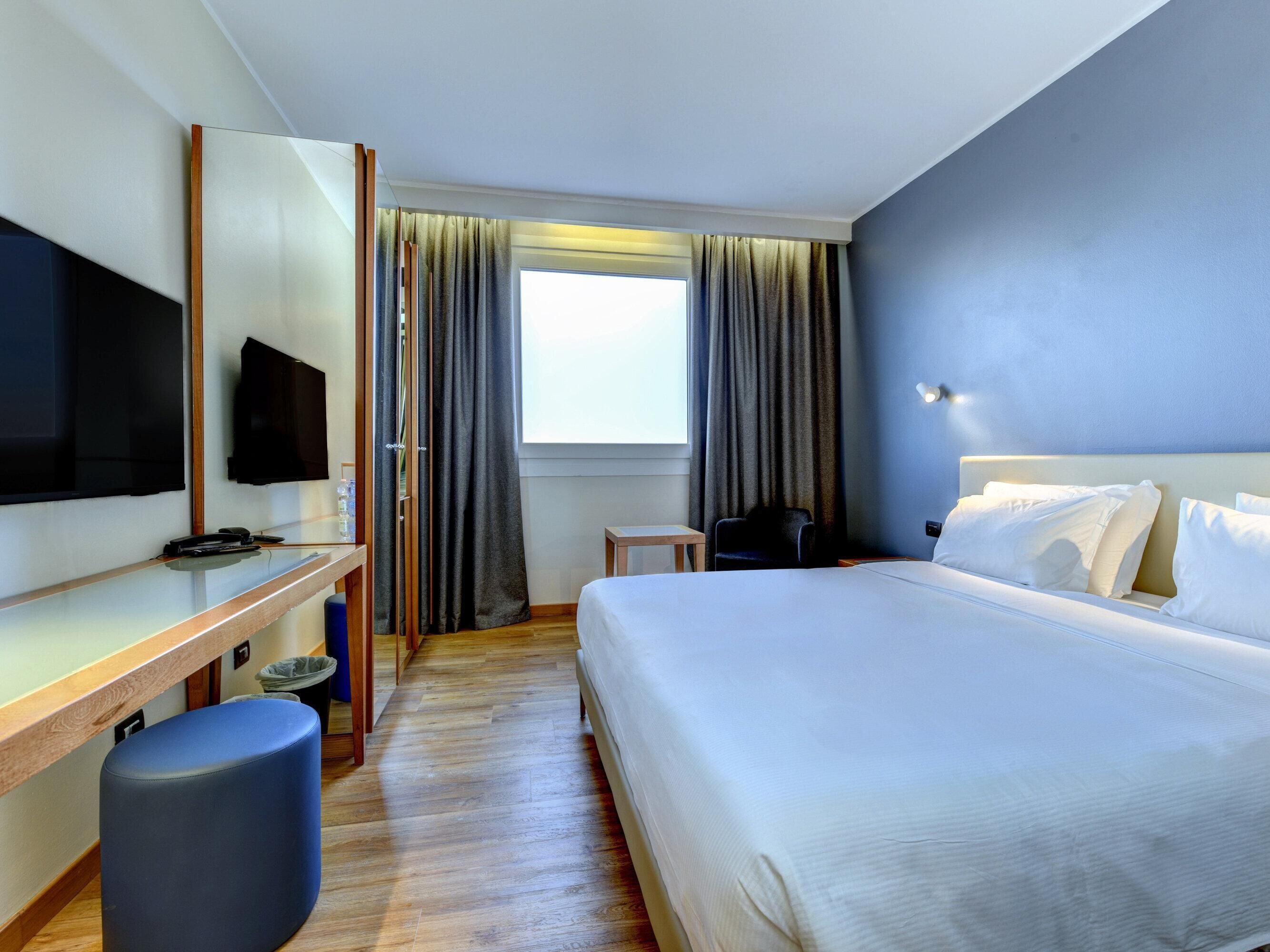 Habitación de hotel con cama, escritorio con televisor de pantalla plana, una silla y una mesita.