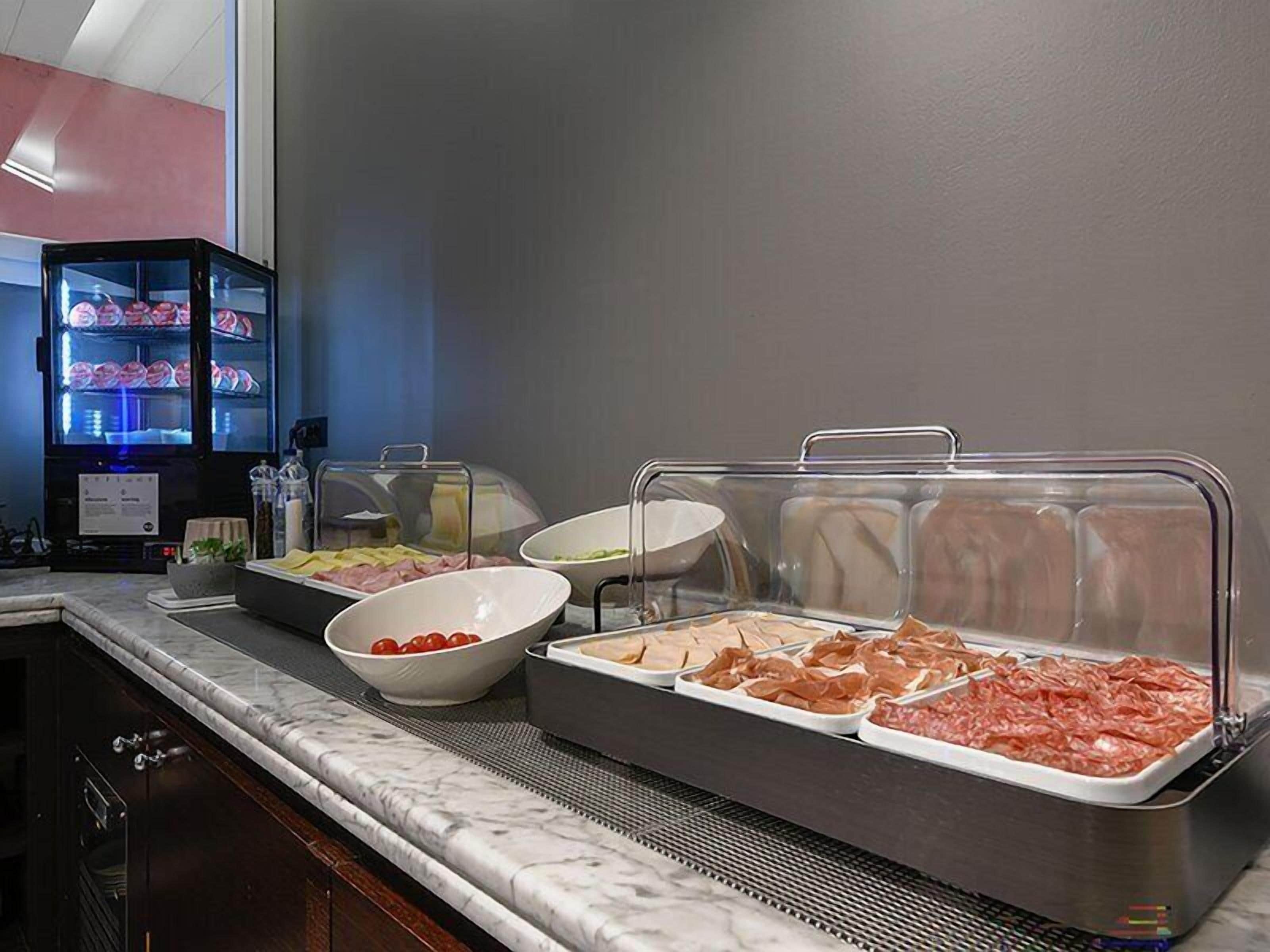 Disposición de un bufé con diversos alimentos en recipientes transparentes, un refrigerador con provisiones y un microondas.