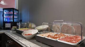 Ein reichhaltiges Buffet mit verschiedenen Speisen in durchsichtigen Behältern, ein Kühlschrank mit Lebensmitteln und eine Mikrowelle.
