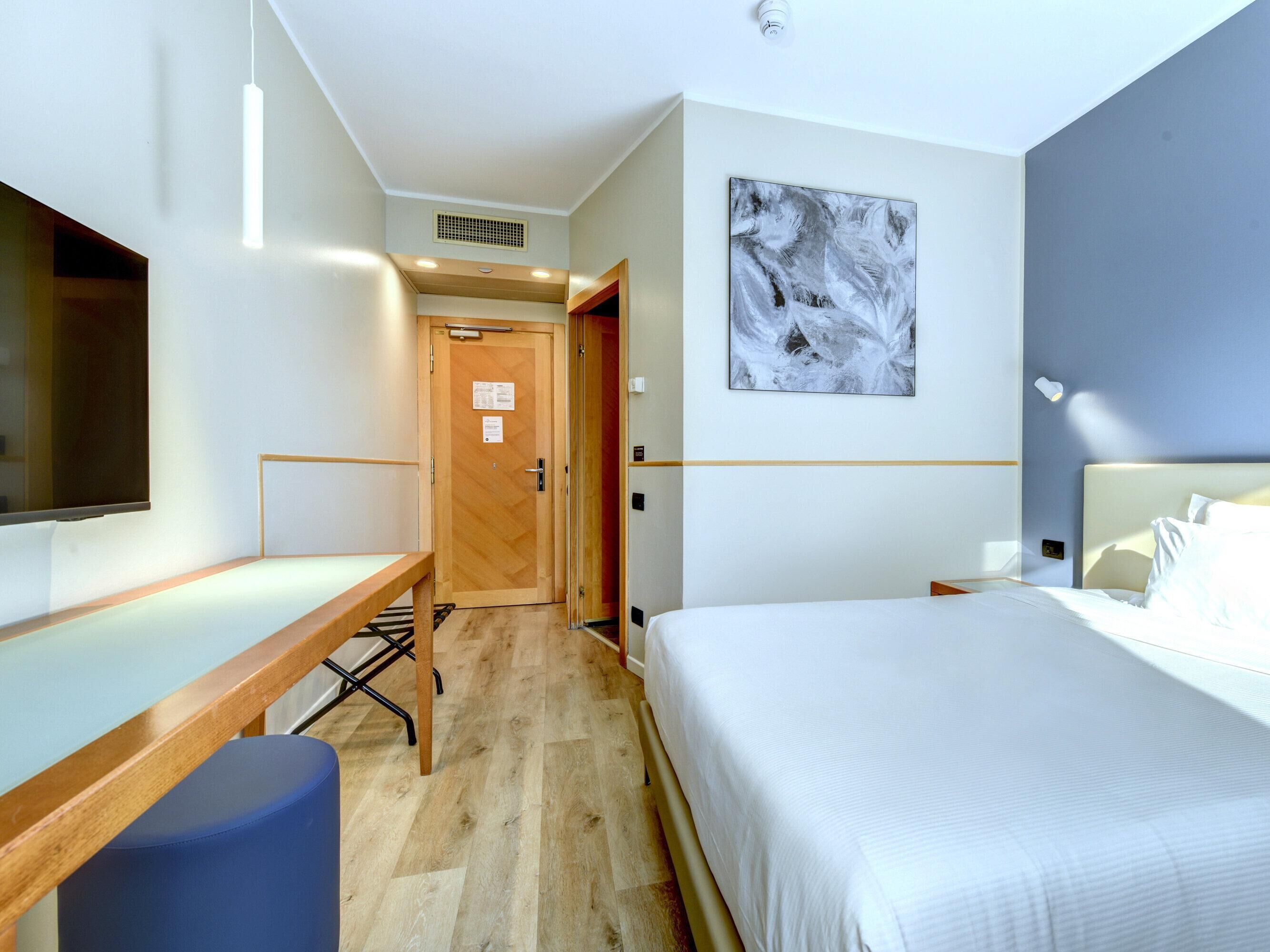 Une chambre d’hôtel avec un lit, un bureau, une chaise, une télévision et un tableau au mur.