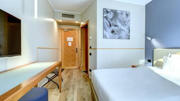 A hotel room with a bed, a desk, a chair, a TV, and a painting on the wall.