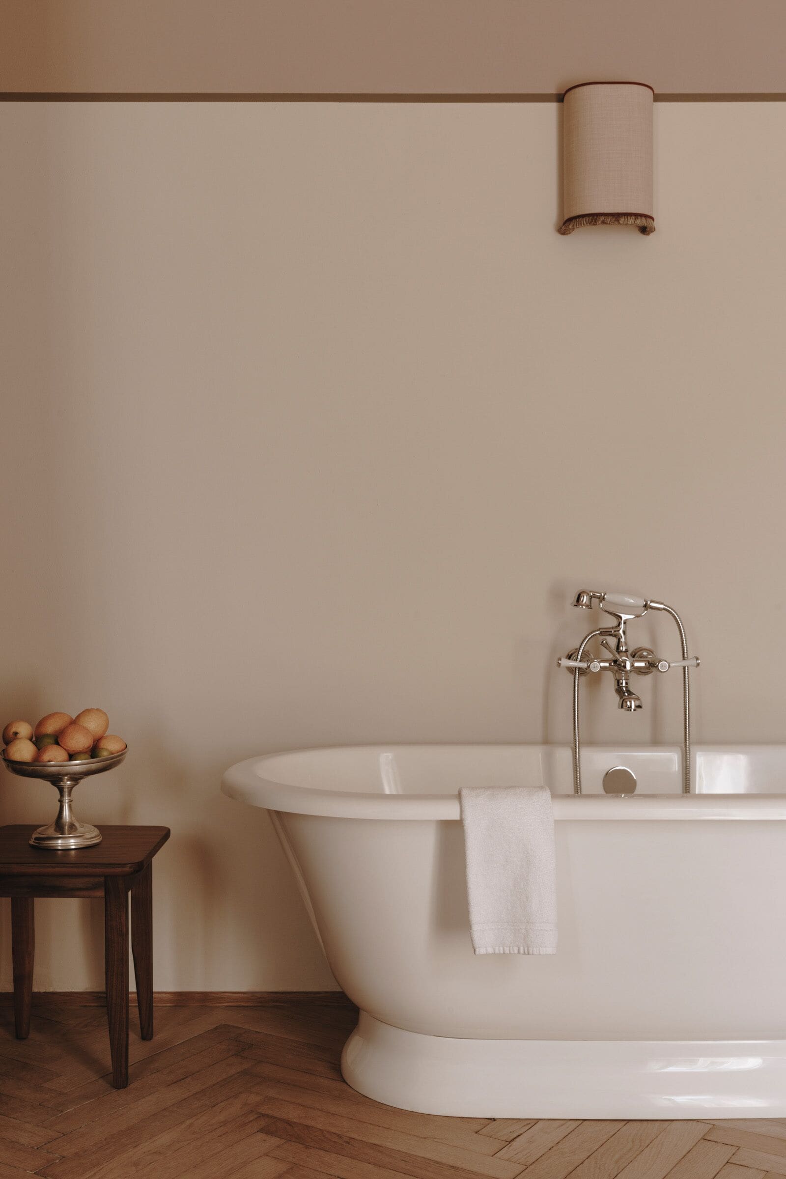 A bathroom with a freestanding bathtub, a small wooden stool with a bowl of eggs, and a towel hanging on the tub.