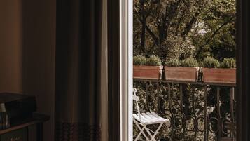Uma porta de correr de vidro aberta dá para um alpendre externo com deck de madeira, uma cadeira branca e guarda-corpo de metal.