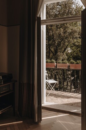 Une porte-fenêtre coulissante donne sur une terrasse extérieure dotée d’une plateforme en bois, d’une chaise blanche et d’une rambarde en métal.