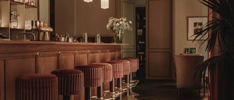 Un espace bar avec des tabourets de bar en bois, un miroir et des luminaires suspendus.