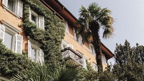 Un immeuble à plusieurs étages doté de balcons, entouré d’une végétation luxuriante, notamment de palmiers.