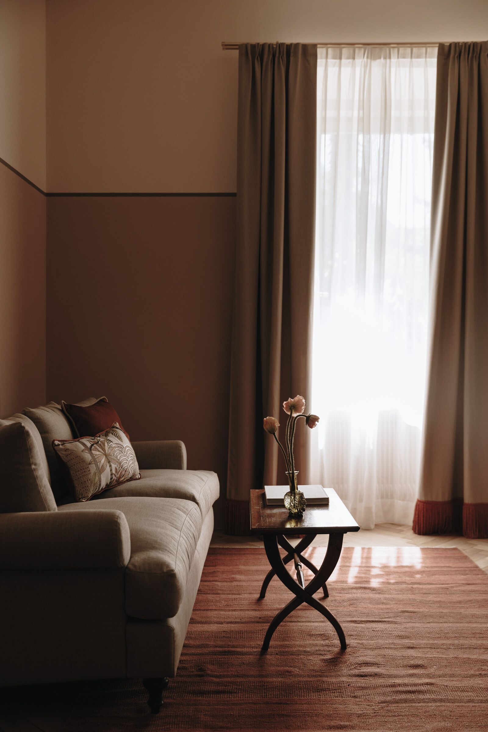 A living room with a sofa, a coffee table with a vase, and a large window with curtains.