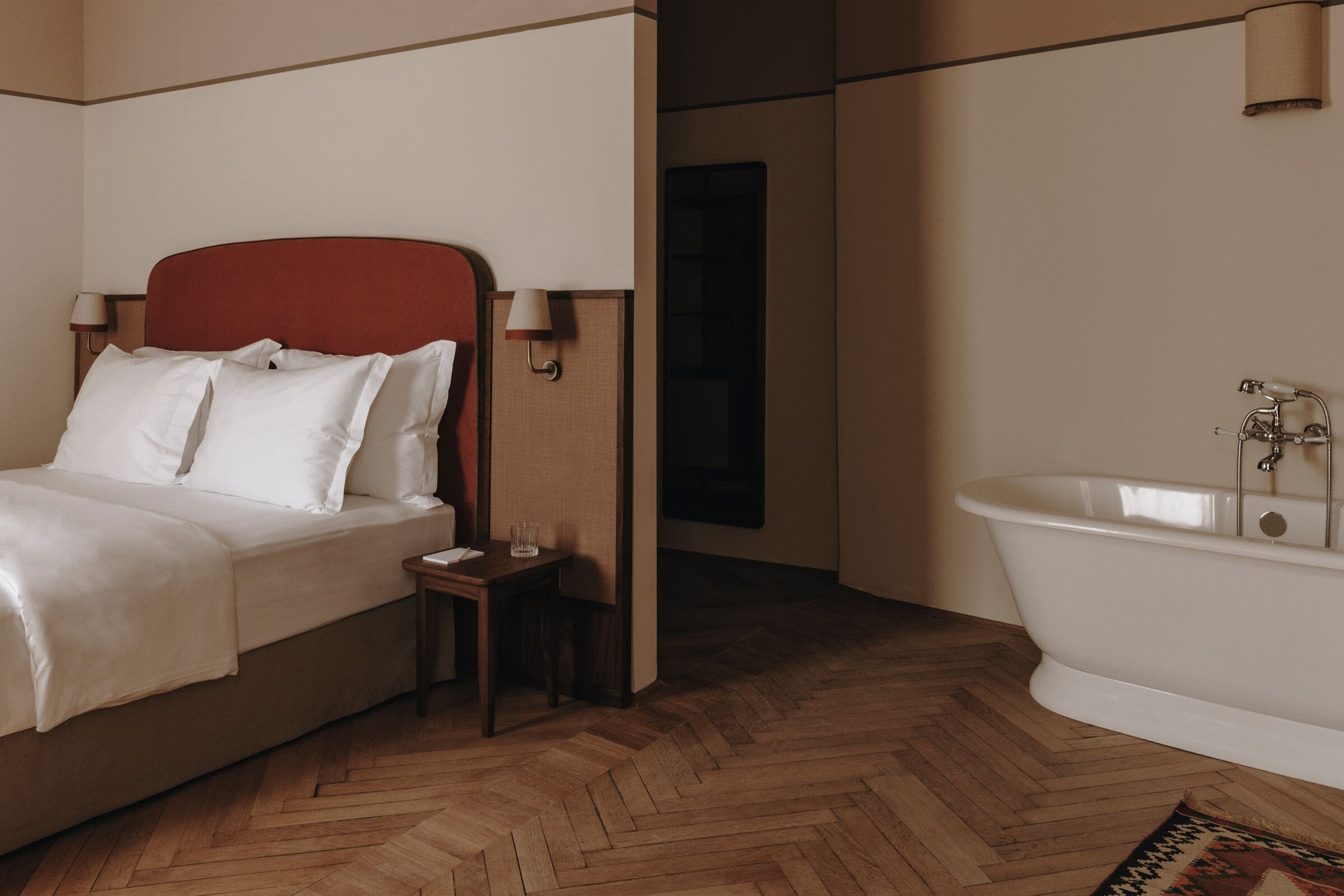 A bedroom with a bed, bedside table, lamp, and a white bathtub.