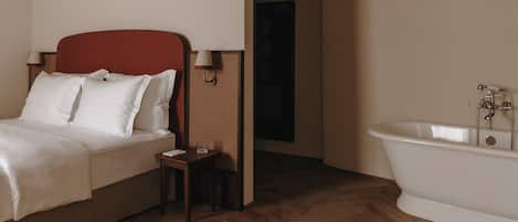 Un dormitorio con cama, mesita de noche, lámpara y una bañera blanca.