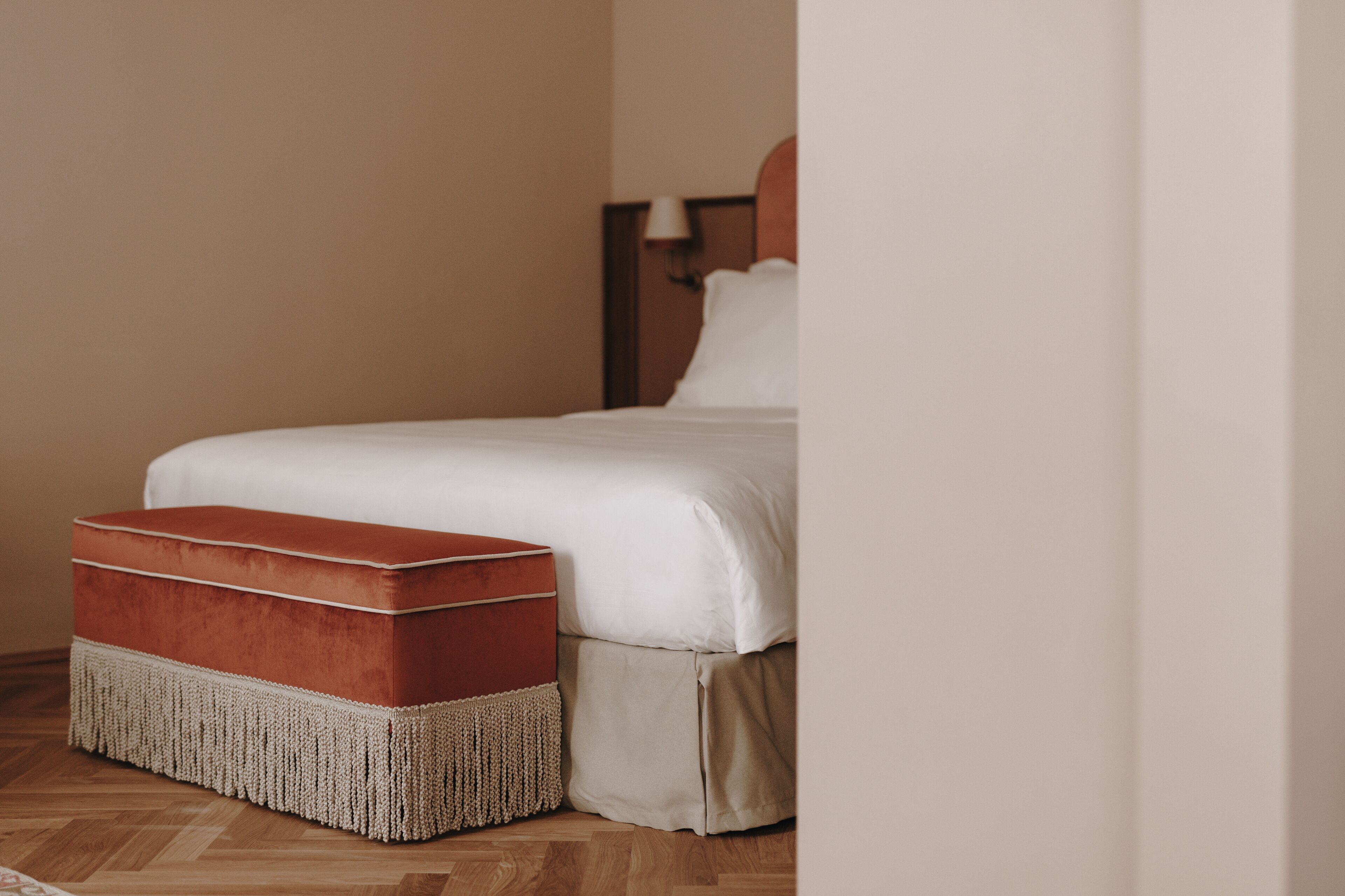 Un letto rifatto con un copriletto bianco e un poggiapiedi imbottito rosso con base intrecciata.