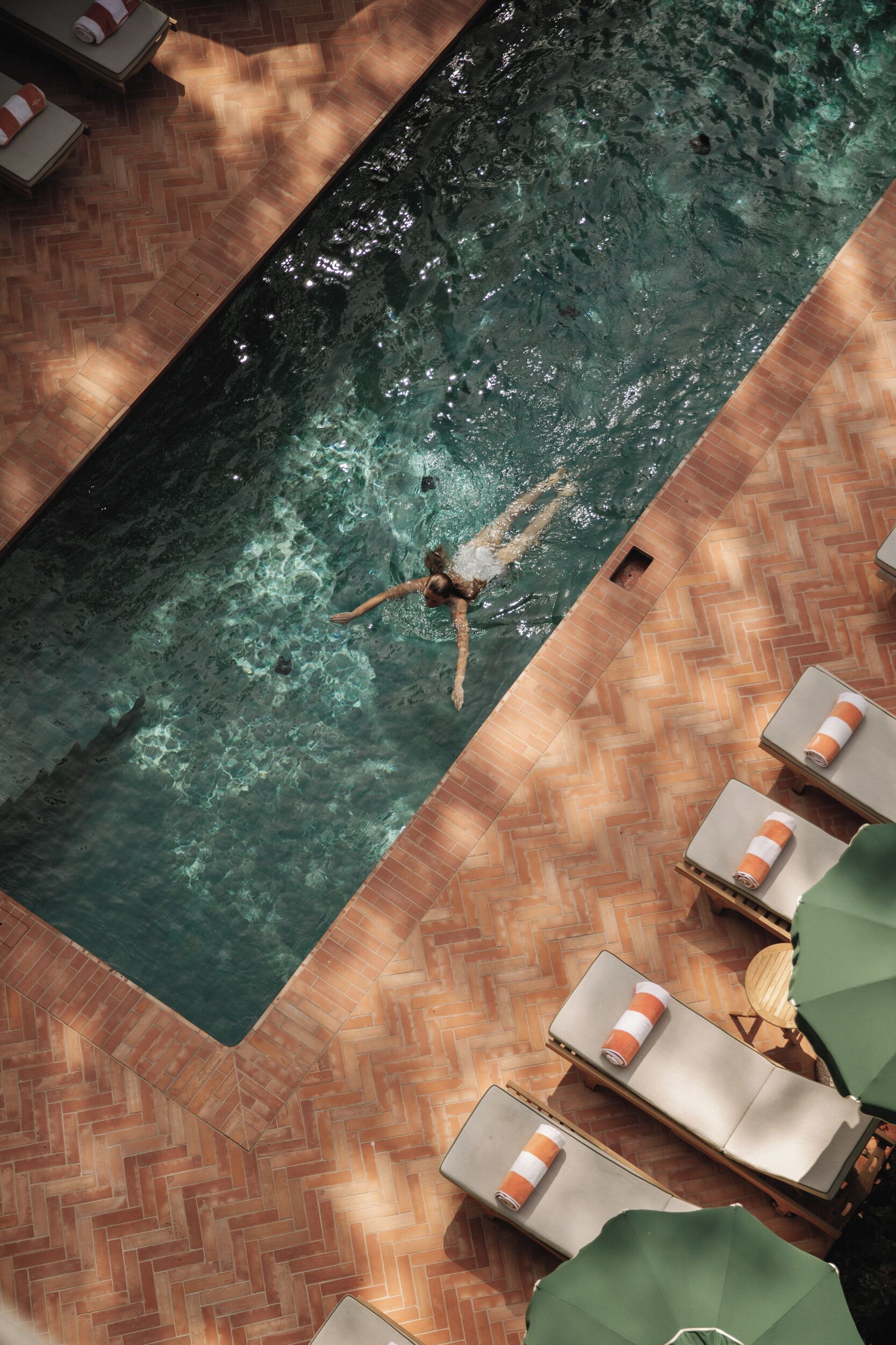 Piscina con diseño de mosaico tipo espiga y sillas de descanso con toallas.