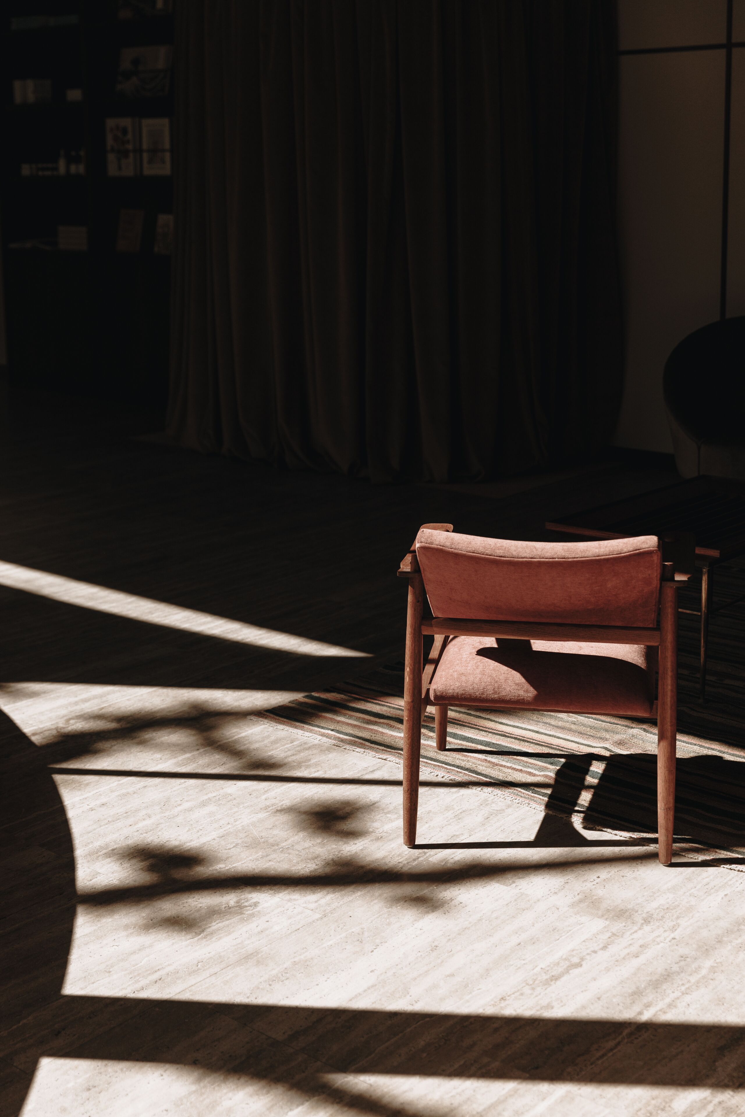 Une chaise dans une pièce faiblement éclairée, avec un tapis à motifs et un rideau en arrière-plan.